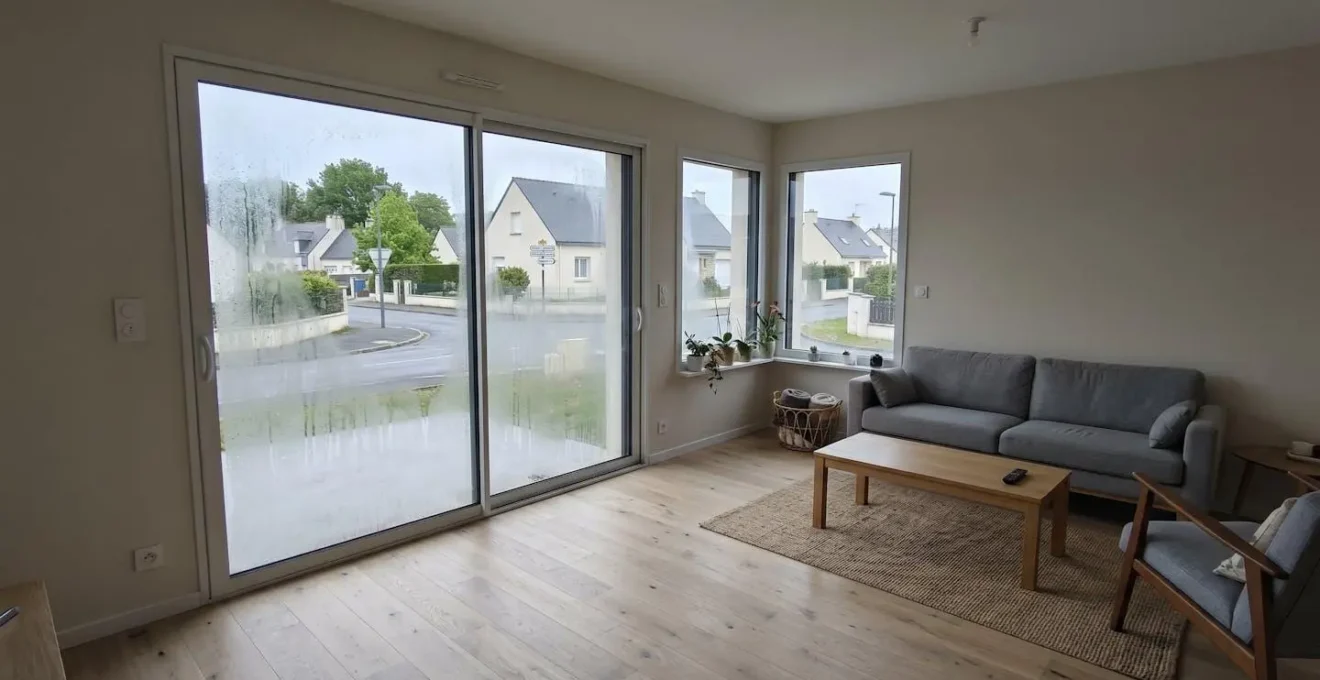 Angle d'une pièce de séjour moderne avec fenêtre récemment installée présentant des traces de condensation sur la vitre, lumière naturelle douce, décor contemporain français