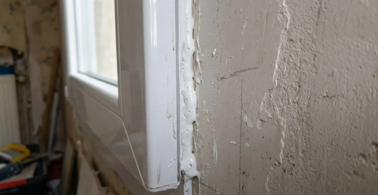 Gros plan sur l'interface entre le dormant d'une fenêtre et le mur, montrant le joint de mousse polyuréthane apparent dans une maison contemporaine